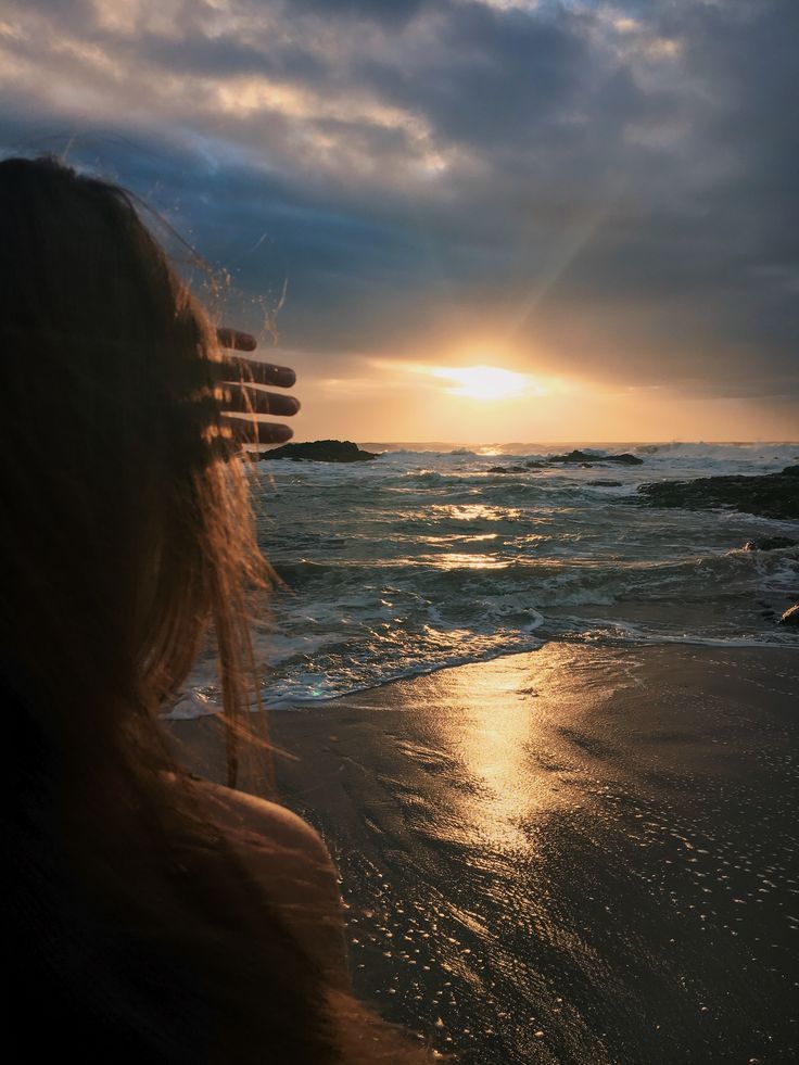 a woman standing on top of a beach next to the ocean under a cloudy sky