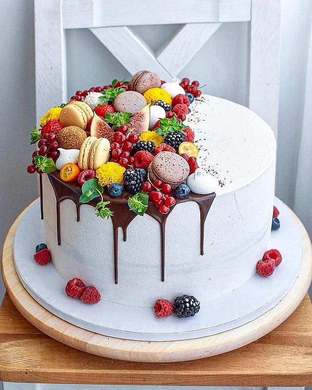 a white cake topped with lots of different types of fruit and chocolate on top of a wooden table