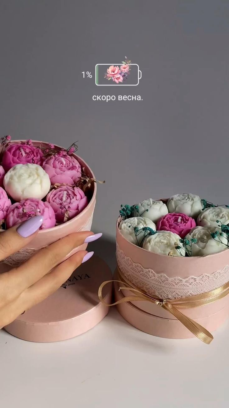 a woman's hand holding a pink and white box filled with flowers