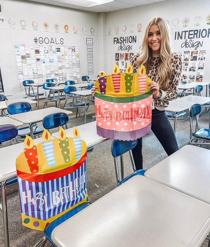 a woman holding up a birthday cake in a classroom