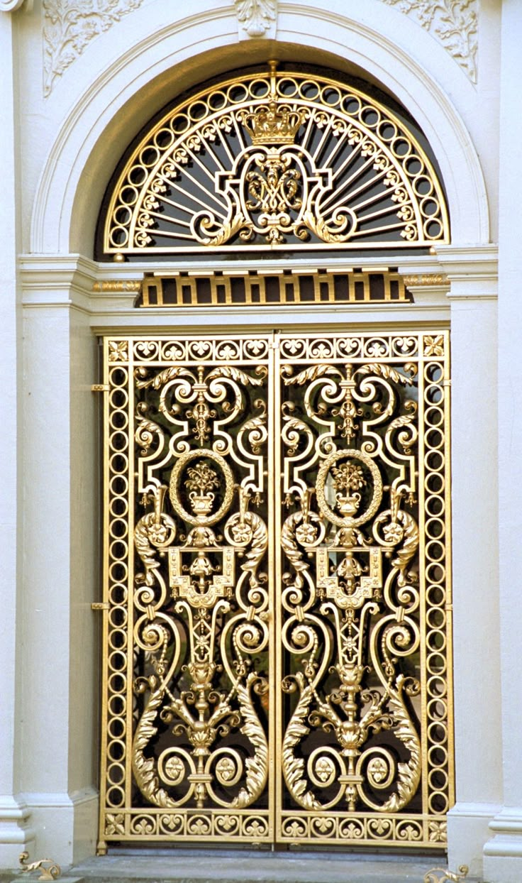 an ornate gold door in the middle of a white building with a clock on it's side