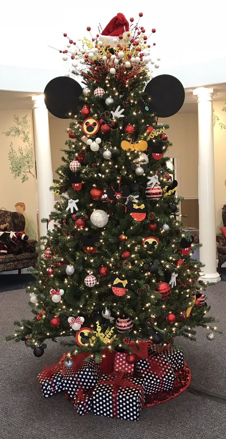 a decorated christmas tree with mickey mouse ears on top and red bows around the base