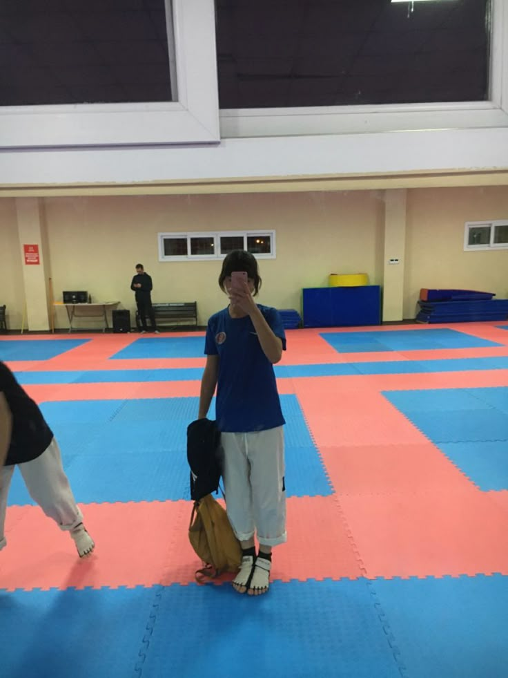 two people standing in a room with blue mats on the floor and one person holding a baseball mitt