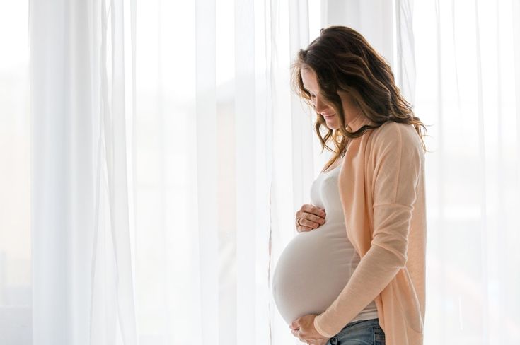 a pregnant woman standing in front of a window with her belly tucked under her stomach