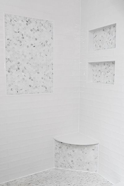 a bathroom with white walls and floor tiles on the shower wall, along with two square niches