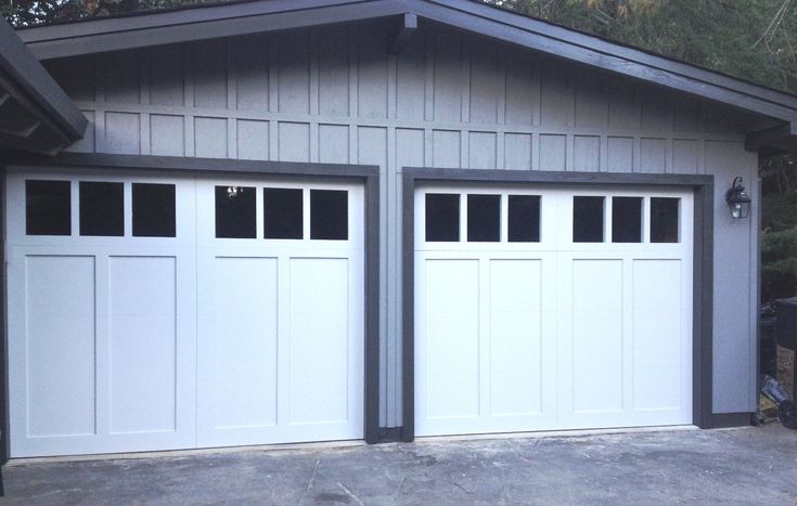 two white garage doors with windows in front of a house