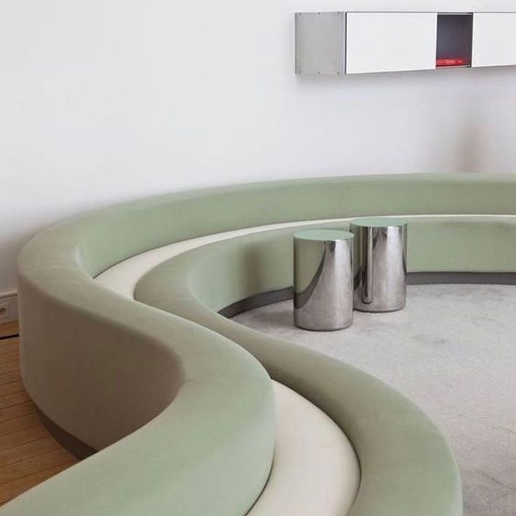 a curved couch with two silver vases on the bottom and a mirror above it