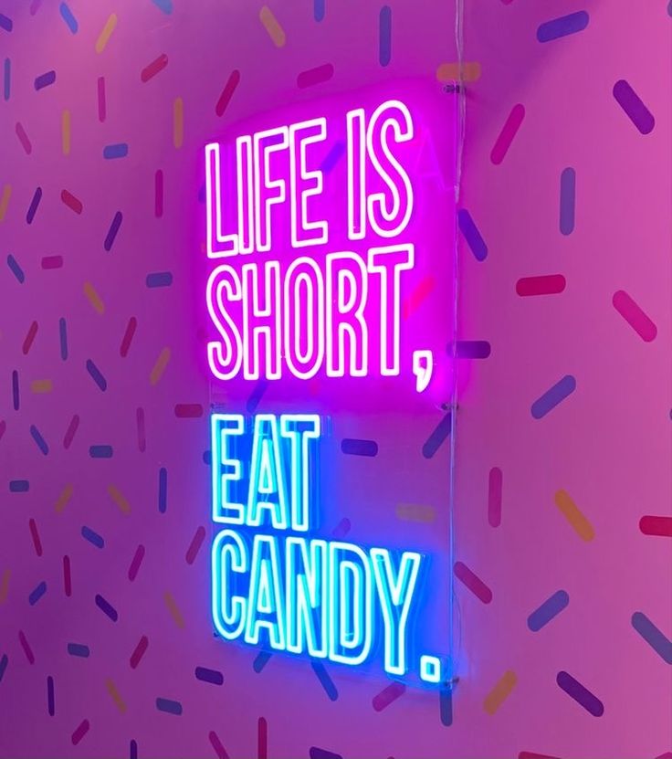 a neon sign that says life is short, eat candy on the wall next to it