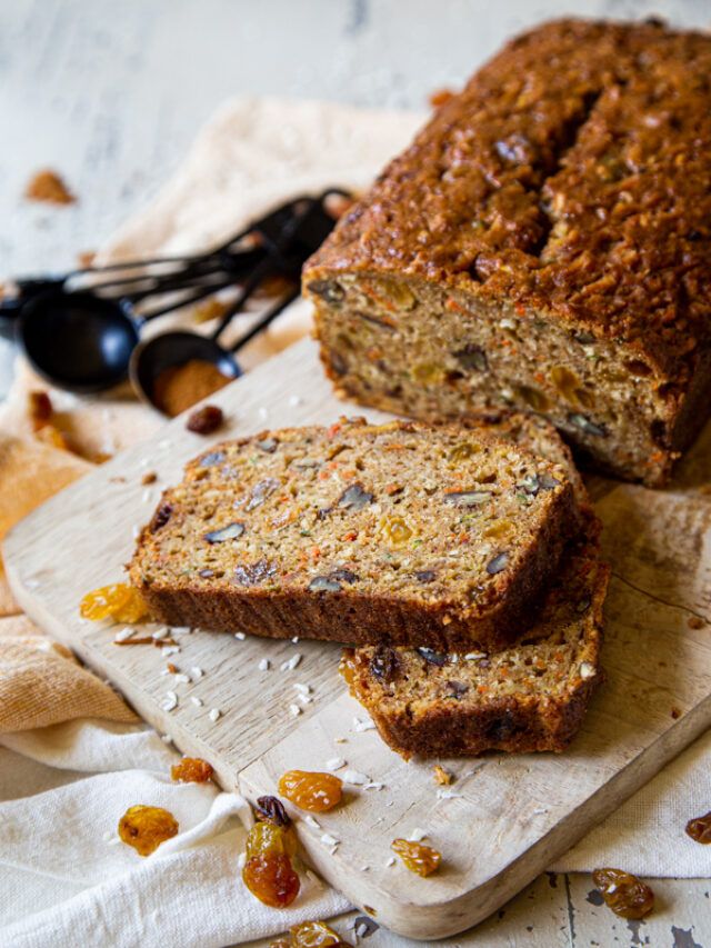 a loaf of banana bread sitting on top of a wooden cutting board next to some raisins