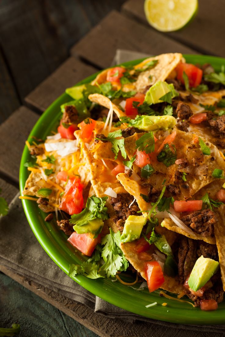 a green plate filled with nachos and salsa on top of a wooden table