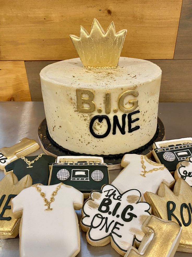 a cake decorated with gold and white icing on top of a table next to cookies