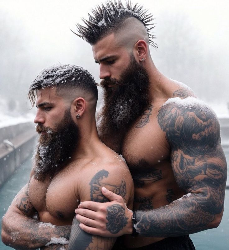 two men standing next to each other with tattoos on their arms and beards in front of a body of water