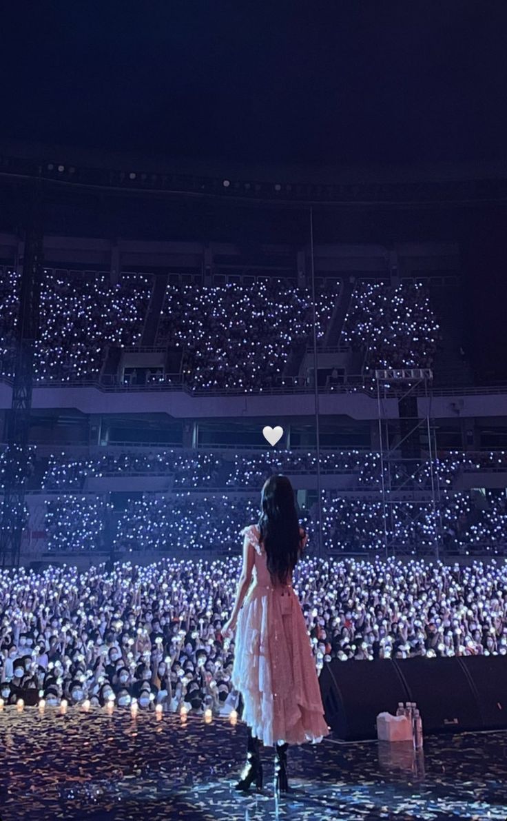 a woman standing in front of a large crowd at night with her back to the camera