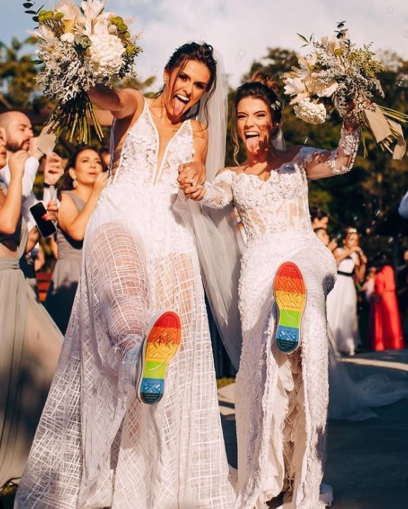 two women in white dresses holding bouquets and standing next to each other with their feet on the ground