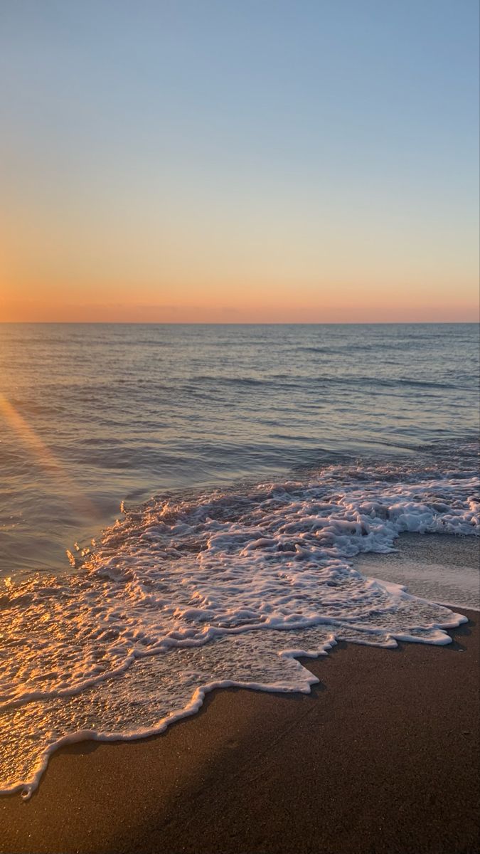 the sun is setting over the ocean with waves crashing onto the beach and sand on the shore