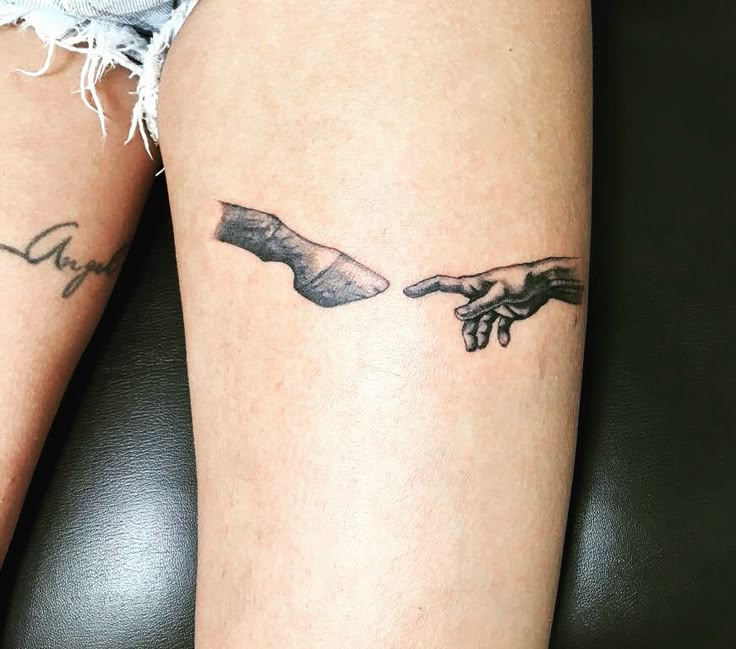 two hands touching each other with tattoos on their arms and legs, one holding the other's hand