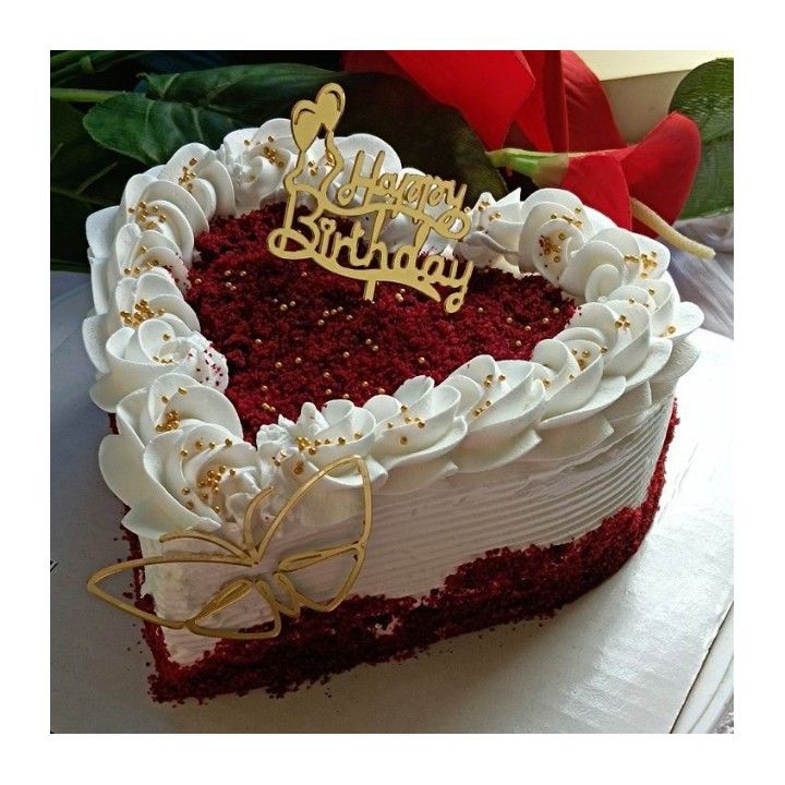 a heart shaped red velvet cake with white frosting and gold decorations on top is sitting on a table