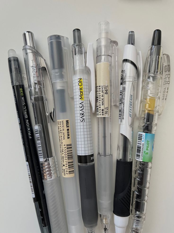 several pens and markers are lined up on a white surface