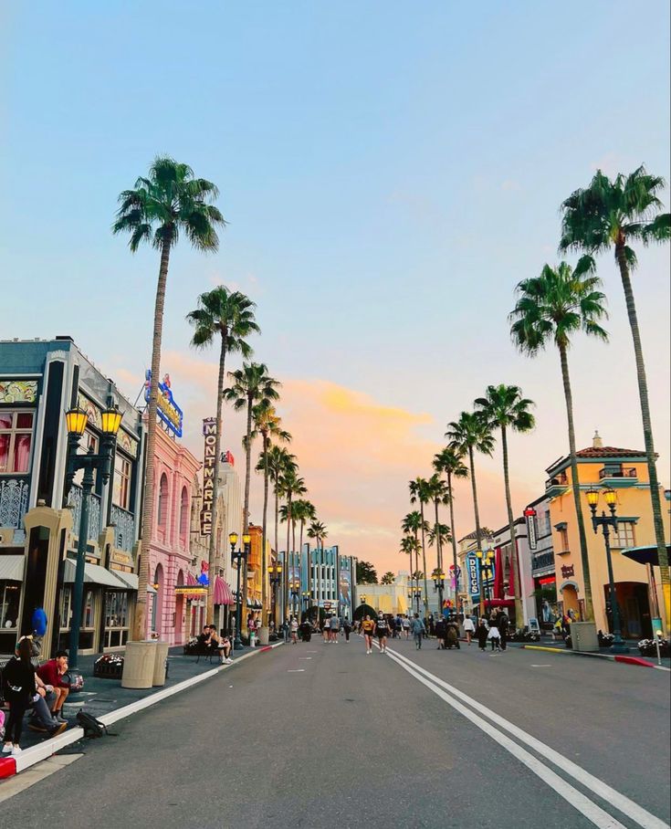 palm trees line the street as people sit on benches in front of buildings and shops