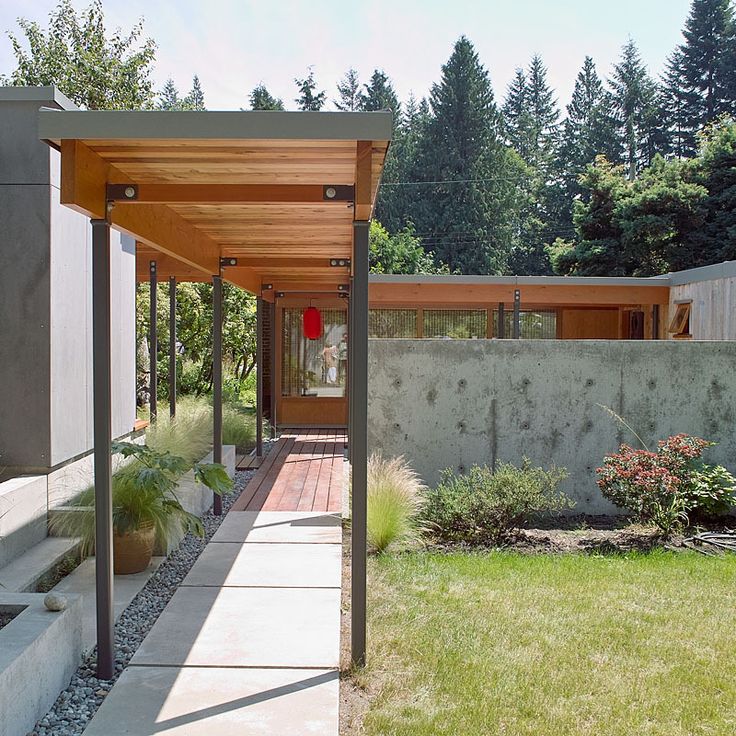 an outdoor covered walkway leading to a house with trees in the backgrouds