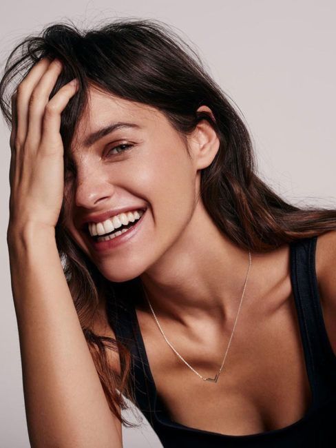 a woman smiling with her hand on her head and wearing a black tank top over her shoulder