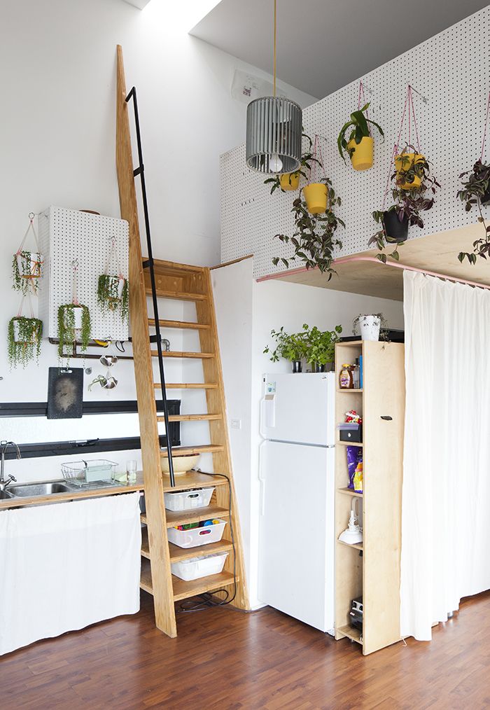 an open kitchen and living room with plants hanging from the ceiling, next to a ladder