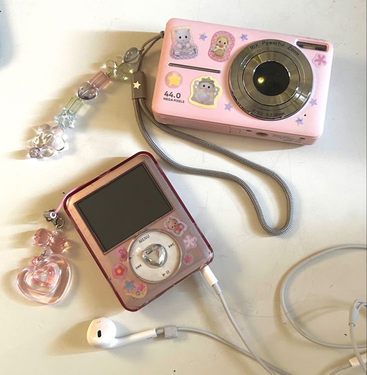 a pink digital camera sitting on top of a table next to ear buds and an mp3 player