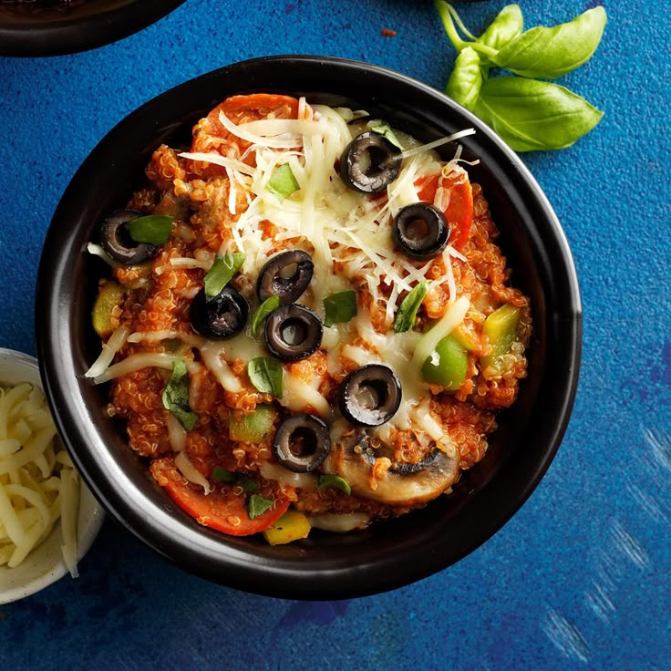 a black bowl filled with pasta and olives on top of a blue tablecloth