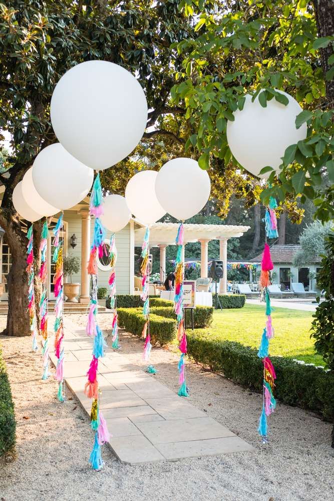 some balloons are hanging from the trees in front of a house with white balls and tassels