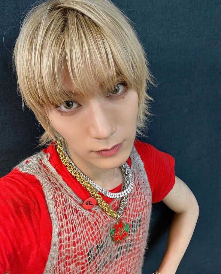 a young man with blonde hair wearing a red shirt and gold chain around his neck