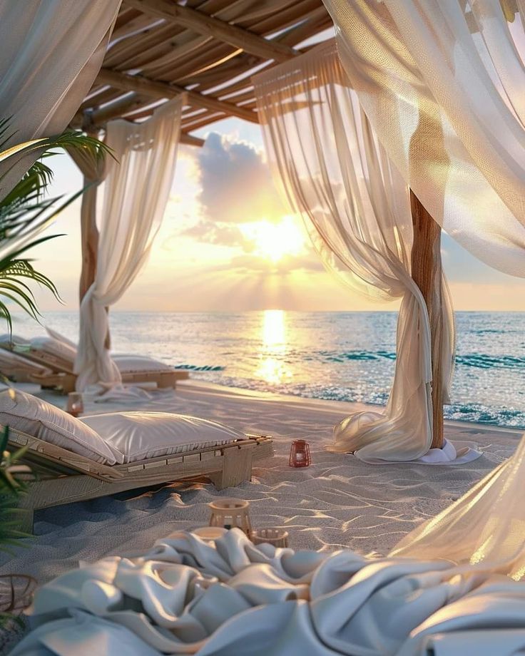 the sun is setting over the ocean with white drapes and pillows on the beach