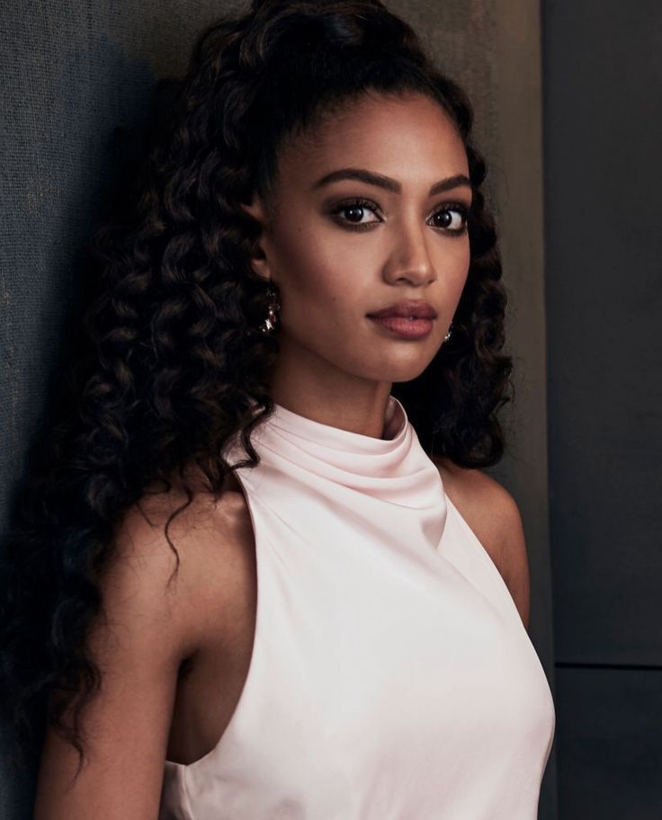 a woman in a white dress leaning against a wall