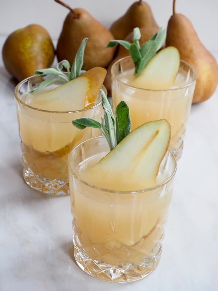 pears and sage are garnished with leaves in glasses on a marble surface