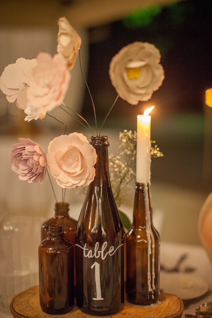 three brown bottles with flowers in them sitting on a wooden table next to a lit candle