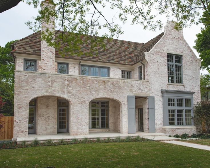 a white brick house with gray shutters on the front and side windows, along with green grass