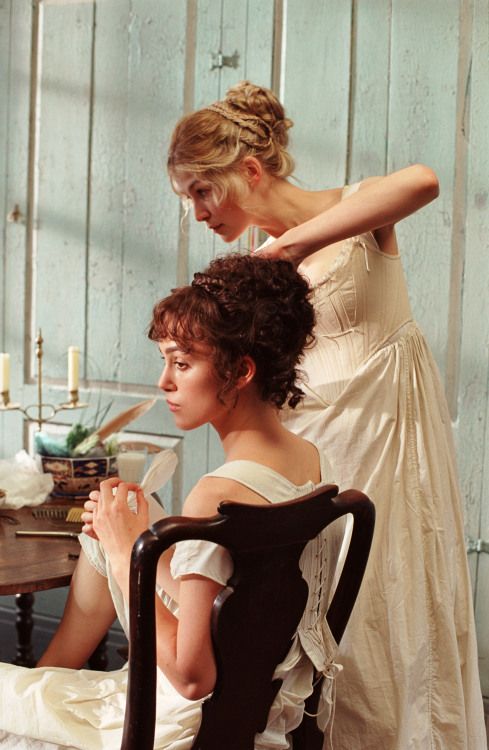 two women in white dresses are sitting at a table and one is touching her hair