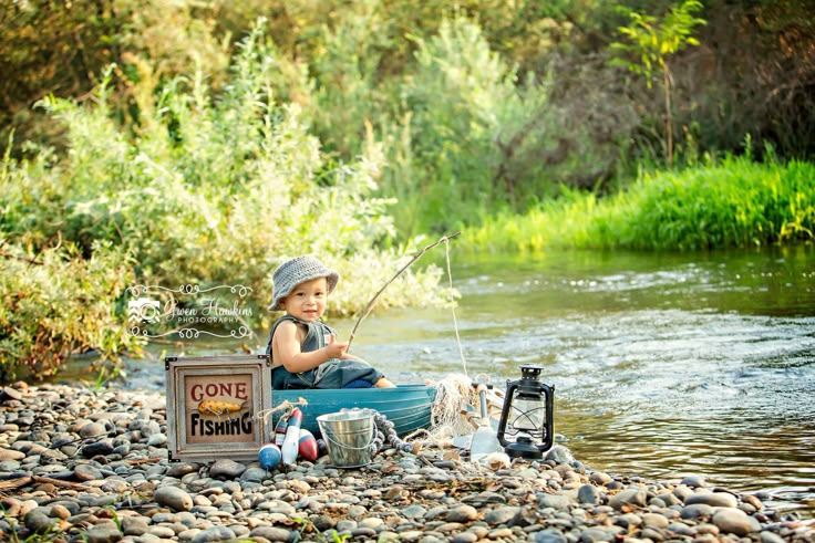 a little boy sitting in a tub with fishing gear on the rocks next to a river