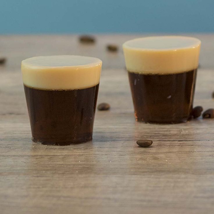 two cups sitting on top of a wooden table filled with coffee beans