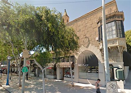 a person is walking down the street in front of a building with trees on both sides