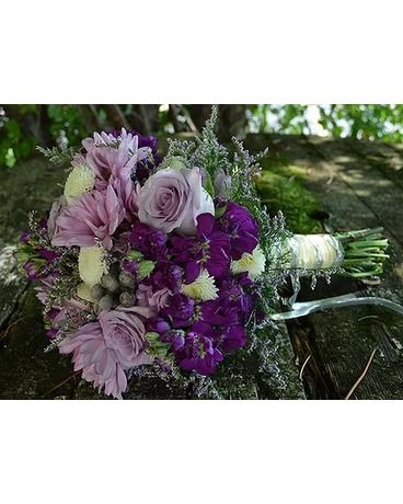 a bouquet of purple and white flowers sitting on top of a wooden table next to a tree