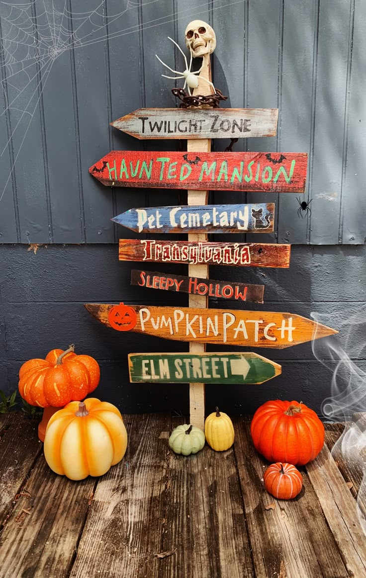 a wooden sign sitting on the side of a building next to pumpkins and gourds