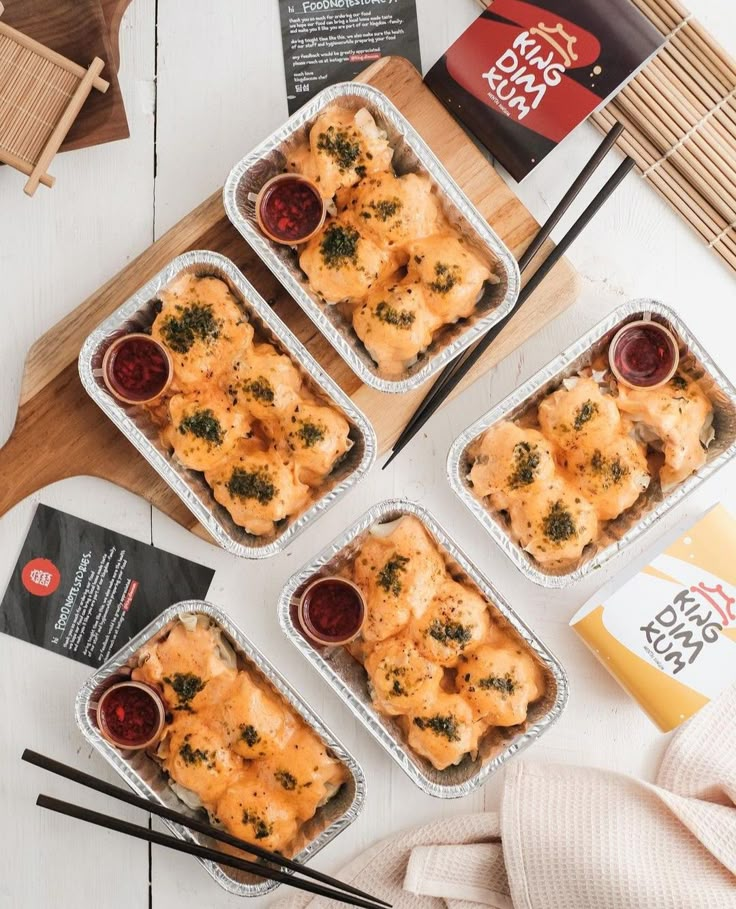 four trays filled with food sitting on top of a wooden table next to chopsticks