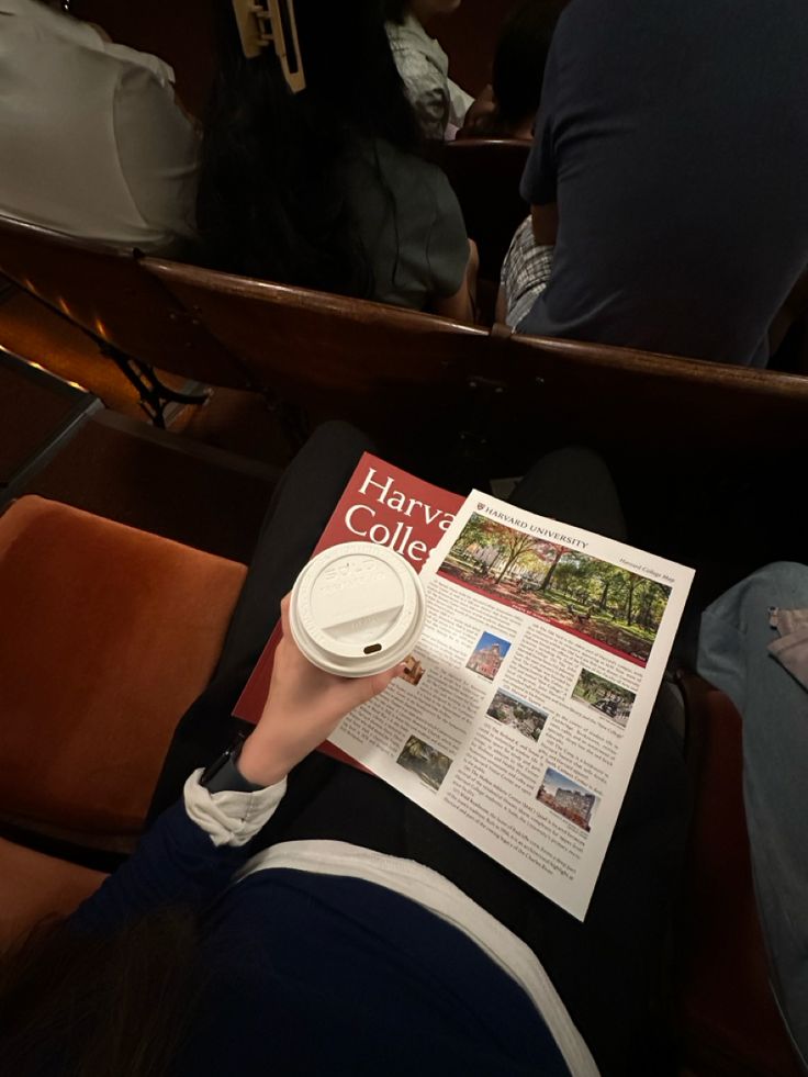 a person sitting in a chair reading a paper with a cup on top of it