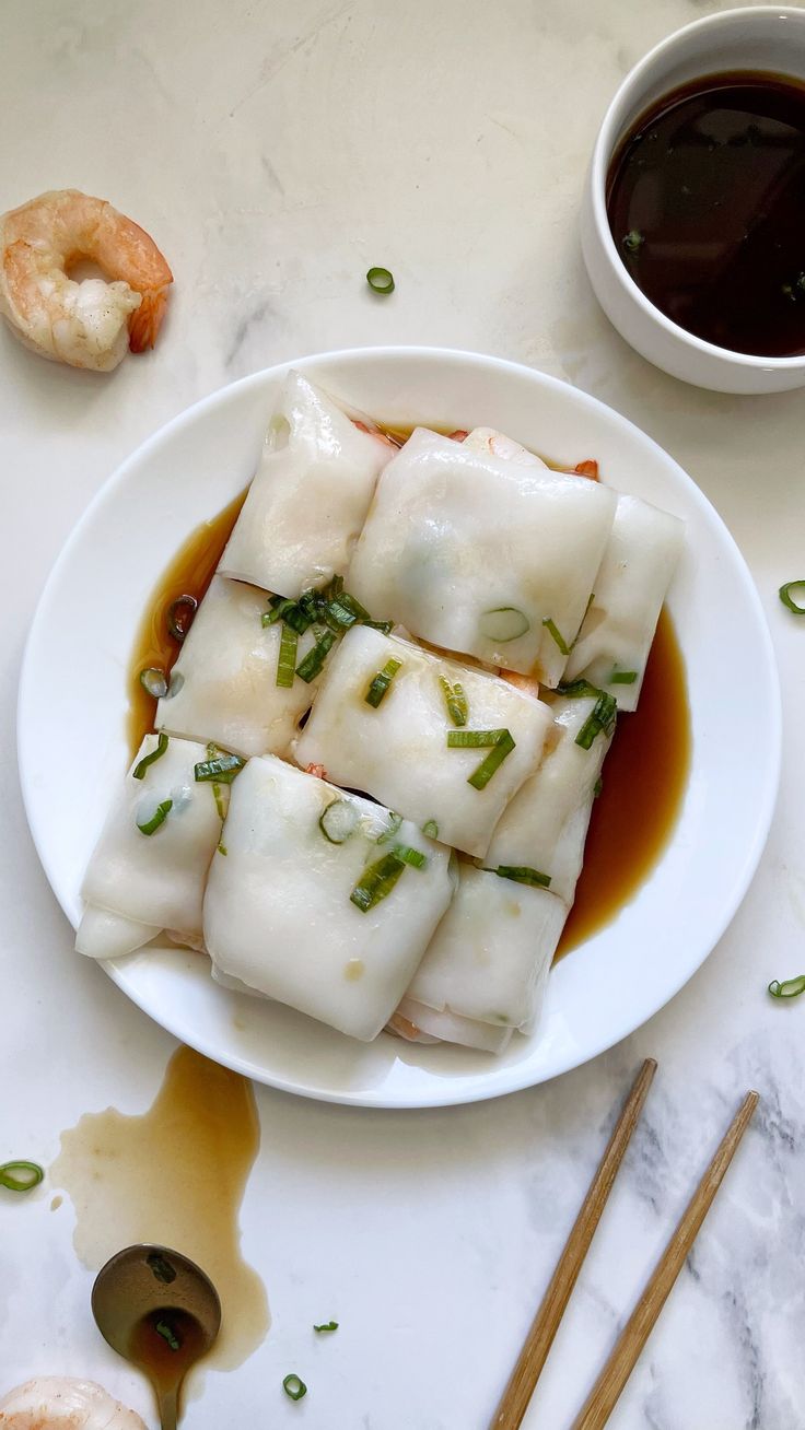 dumplings are served on a white plate with dipping sauce and chopsticks next to them