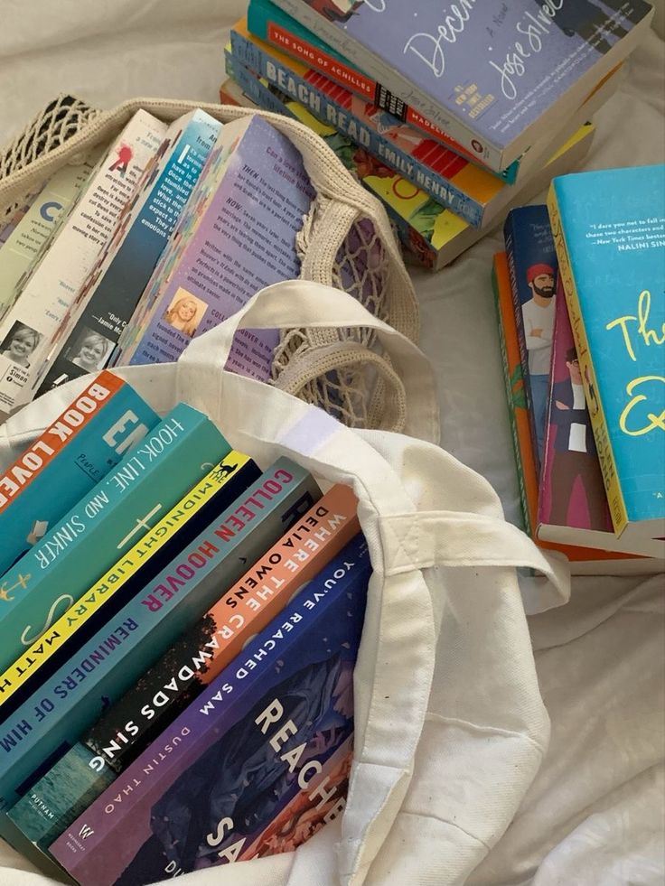 a bag full of books sitting on top of a white bed next to a pile of books