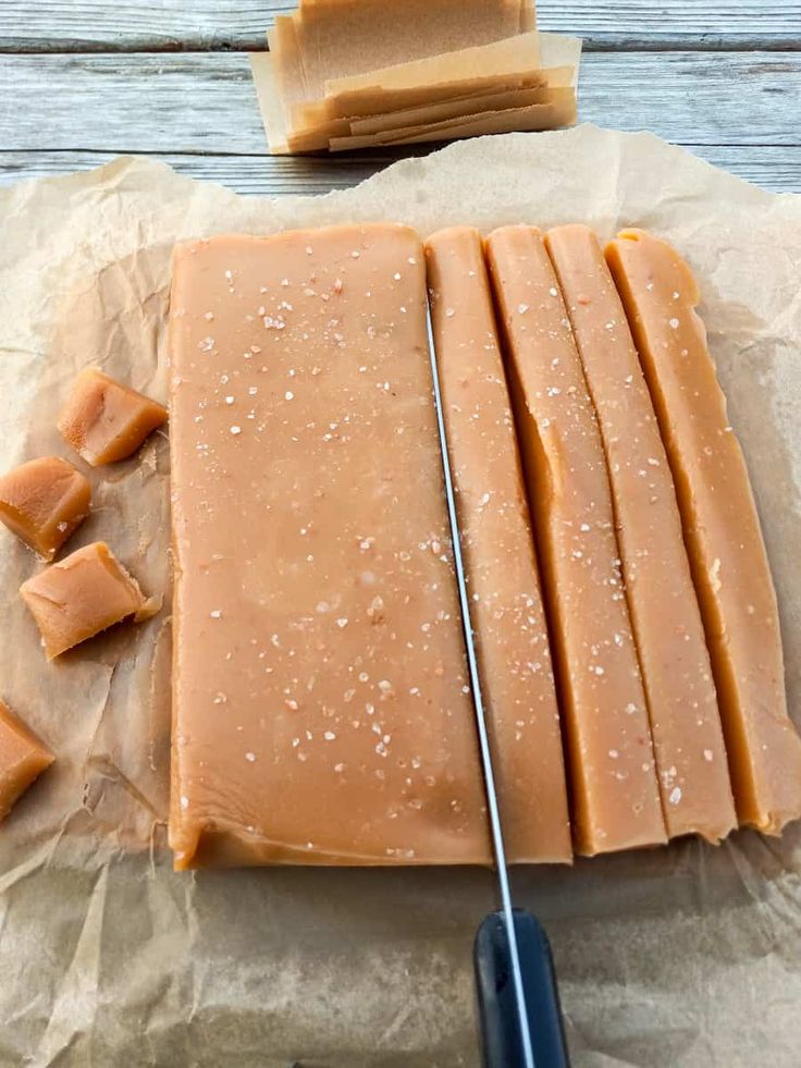 sliced pieces of caramel cheese sitting on top of wax paper next to a knife