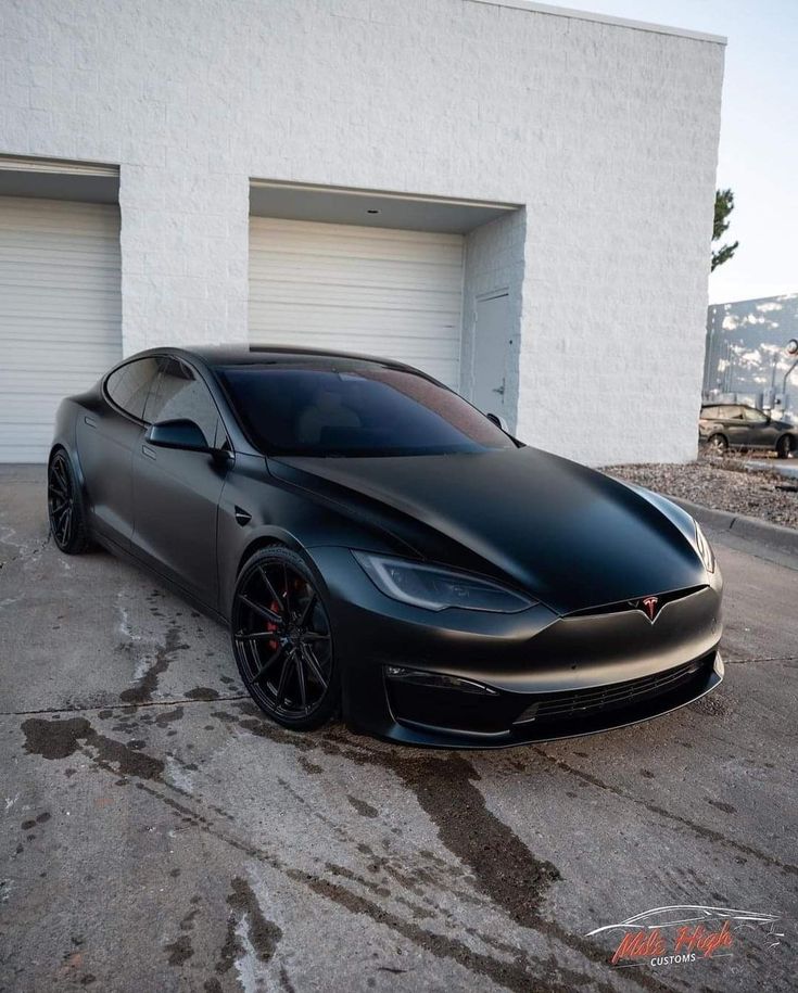 a black tesla parked in front of a garage