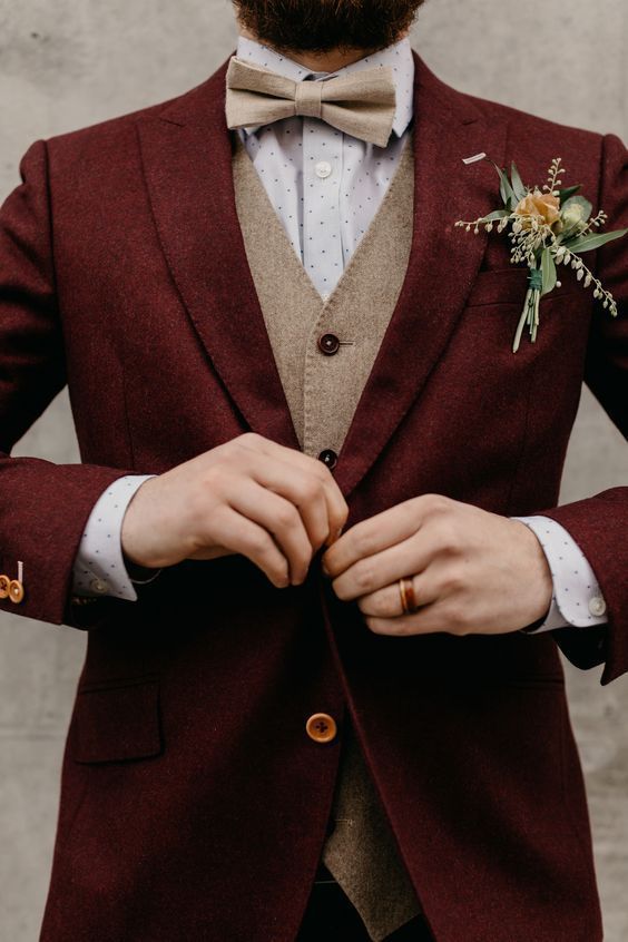 a man in a red suit and bow tie is tying his boutonniere