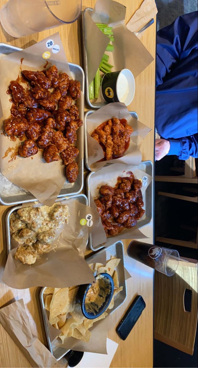 several trays filled with food sitting on top of a wooden table next to a person