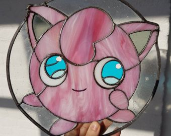 a hand holding up a pink and blue stained glass cat face window decoration with eyes